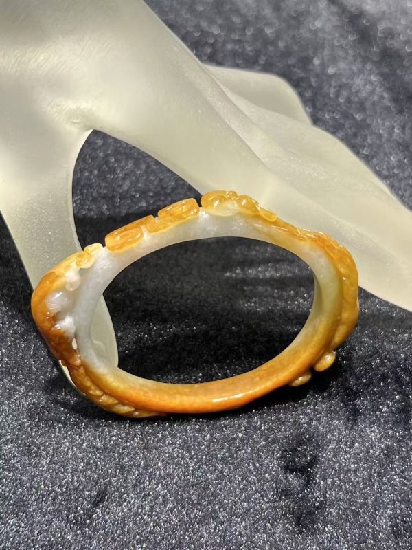 Translucent brownish-yellow jadeite bangle with hand-carved ruyi cloud scroll motifs symbolising fortune and continuity — Nanyang Jade Singapore