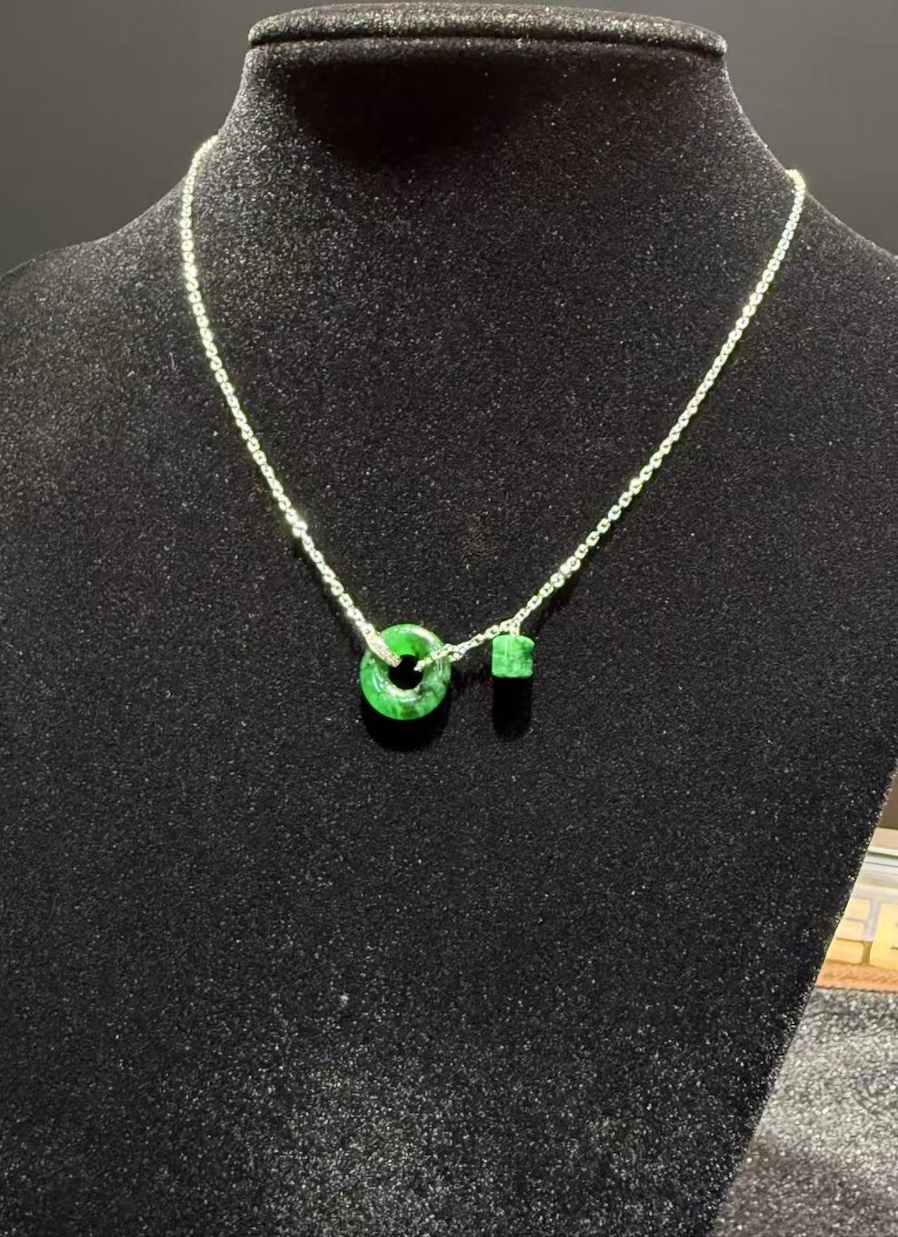 Translucent green jadeite safety knot pendant with dangling jade barrel on 18K white gold chain symbolising peace and protection — Nanyang Jade Singapore