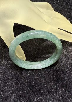 Translucent bluish-green oval jadeite bangle with soft watery tones on black background