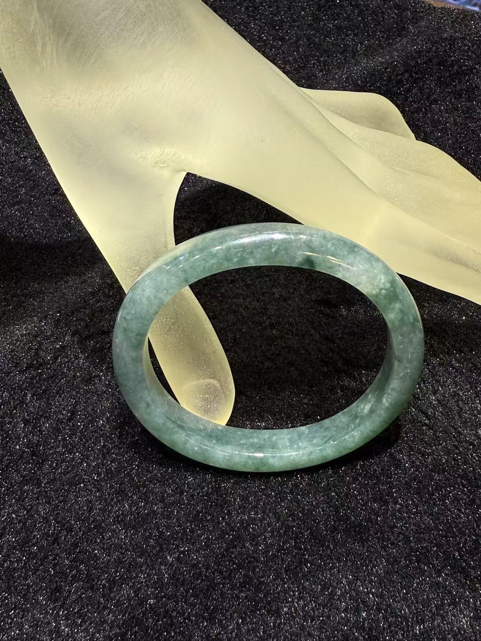 Translucent bluish-green oval jadeite bangle with soft watery tones on black background