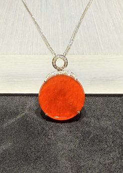 Translucent vibrant red jadeite safety disk pendant set in 18K white gold with diamonds.