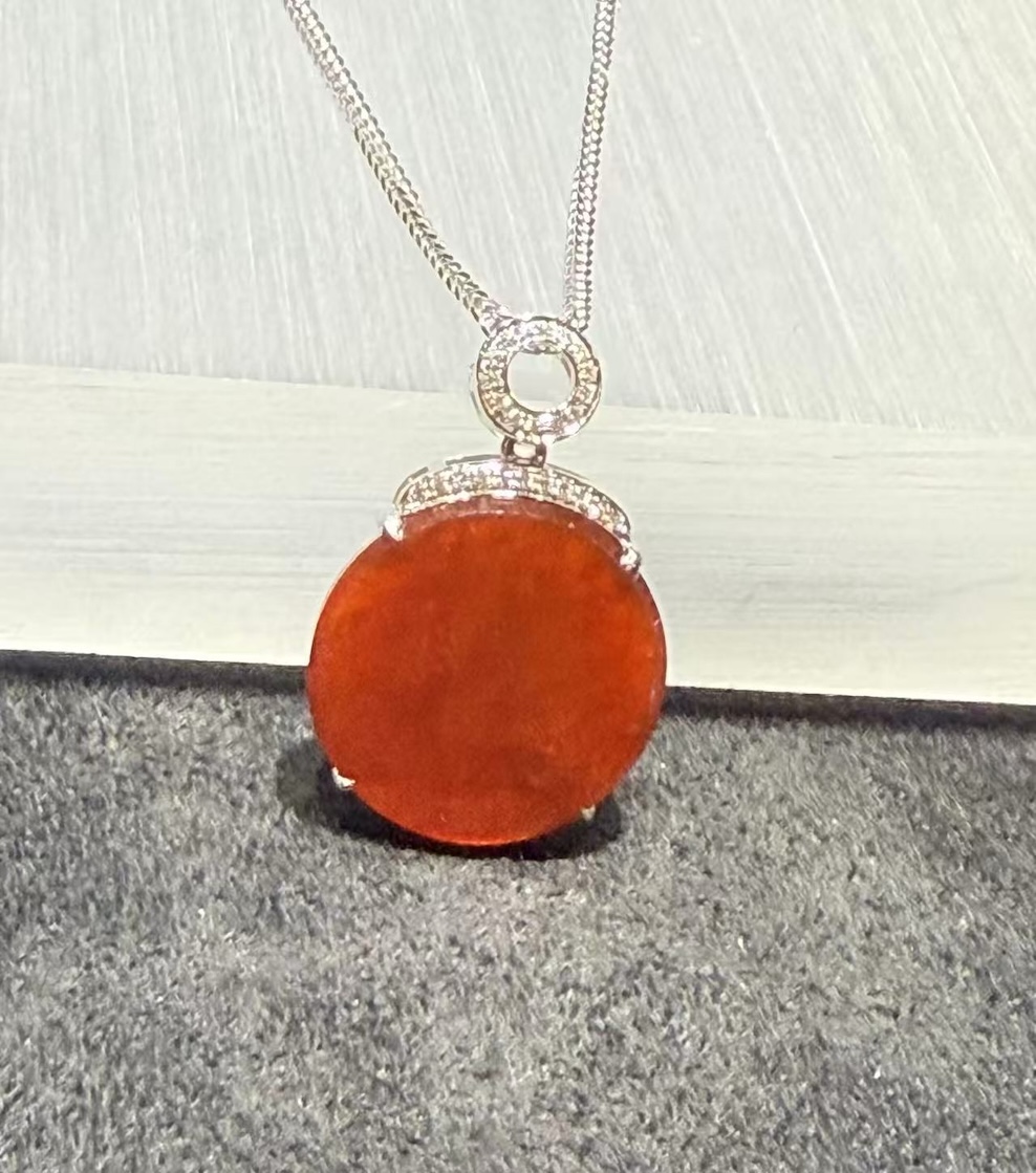 Translucent vibrant red jadeite safety disk pendant set in 18K white gold with diamonds.