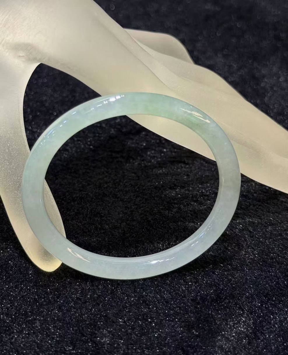 Icy jadeite bangle with a highly translucent body and a faint green wash, carved in a round cut from a single piece of jade