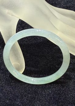 Icy jadeite bangle with a highly translucent body and a faint green wash, carved in a round cut from a single piece of jade