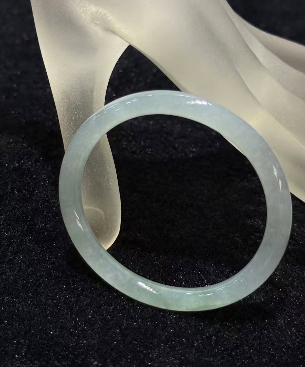 Icy jadeite bangle with a highly translucent body and a faint green wash, carved in a round cut from a single piece of jade