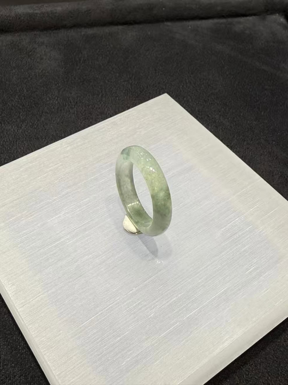 Icy jade ring carved from a single piece of translucent jadeite, with soft green floating-flower patches drifting through a clear, glassy band, shown on a white display stand