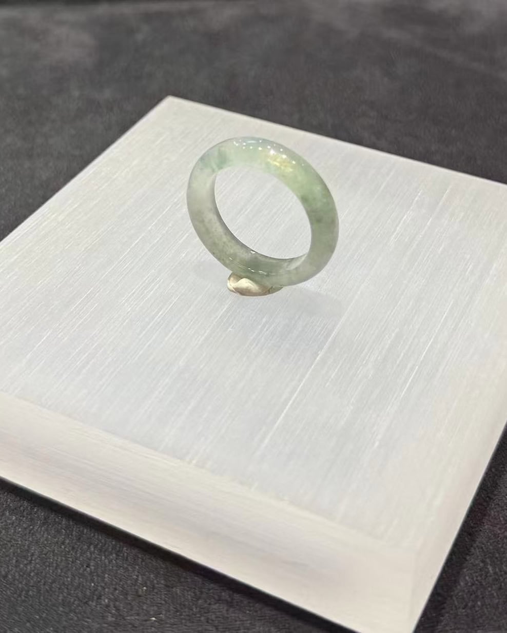Icy jade ring carved from a single piece of translucent jadeite, with soft green floating-flower patches drifting through a clear, glassy band, shown on a white display stand