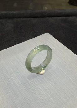 Icy jade ring carved from a single piece of translucent jadeite, with soft green floating-flower patches drifting through a clear, glassy band, shown on a white display stand