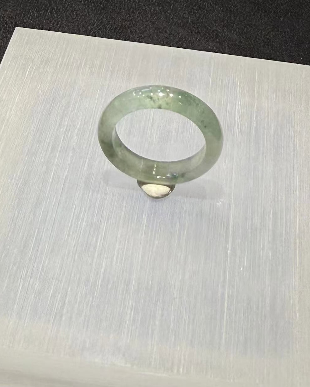 Icy jade ring carved from a single piece of translucent jadeite, with soft green floating-flower patches drifting through a clear, glassy band, shown on a white display stand