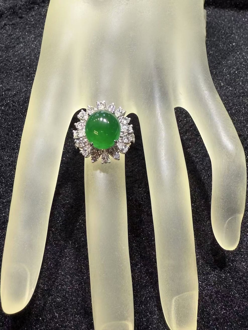 Vivid green jade cabochon ring set in 18k white gold with a brilliant-cut diamond sunburst halo, displayed on a frosted hand stand against black velvet