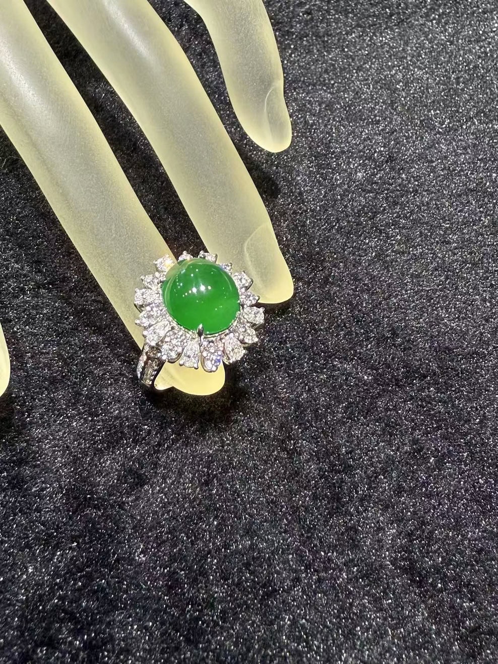 Vivid green jade cabochon ring set in 18k white gold with a brilliant-cut diamond sunburst halo, displayed on a frosted hand stand against black velvet