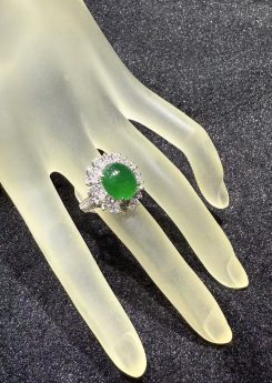 Vivid green jade cabochon ring set in 18k white gold with a brilliant-cut diamond sunburst halo, displayed on a frosted hand stand against black velvet