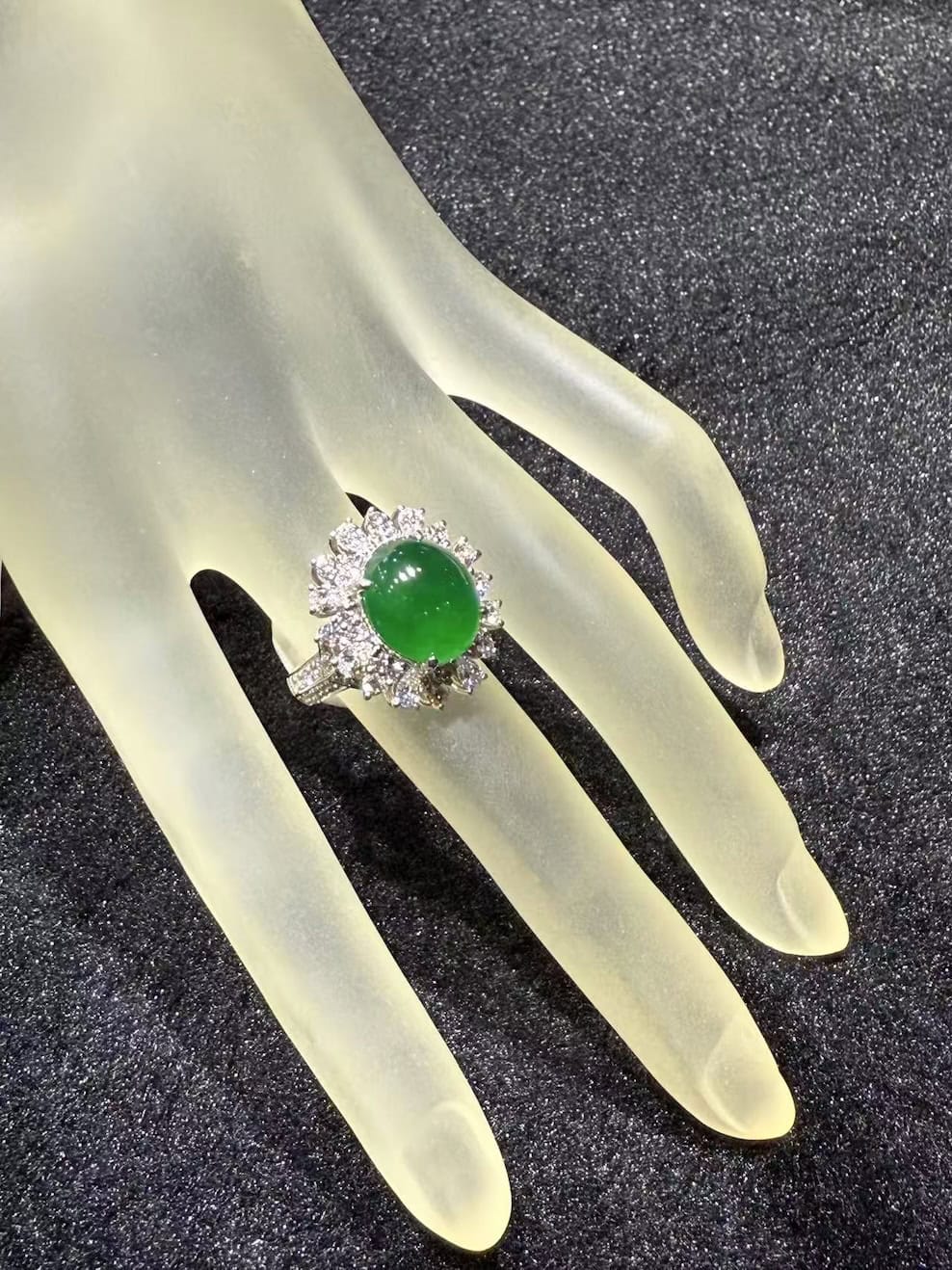 Vivid green jade cabochon ring set in 18k white gold with a brilliant-cut diamond sunburst halo, displayed on a frosted hand stand against black velvet