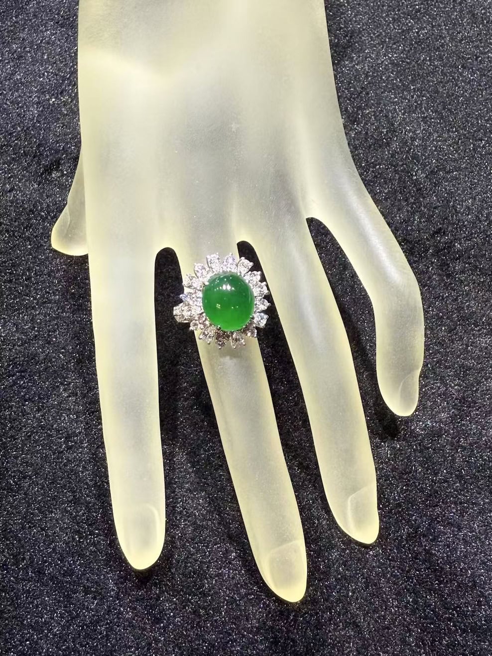 Vivid green jade cabochon ring set in 18k white gold with a brilliant-cut diamond sunburst halo, displayed on a frosted hand stand against black velvet
