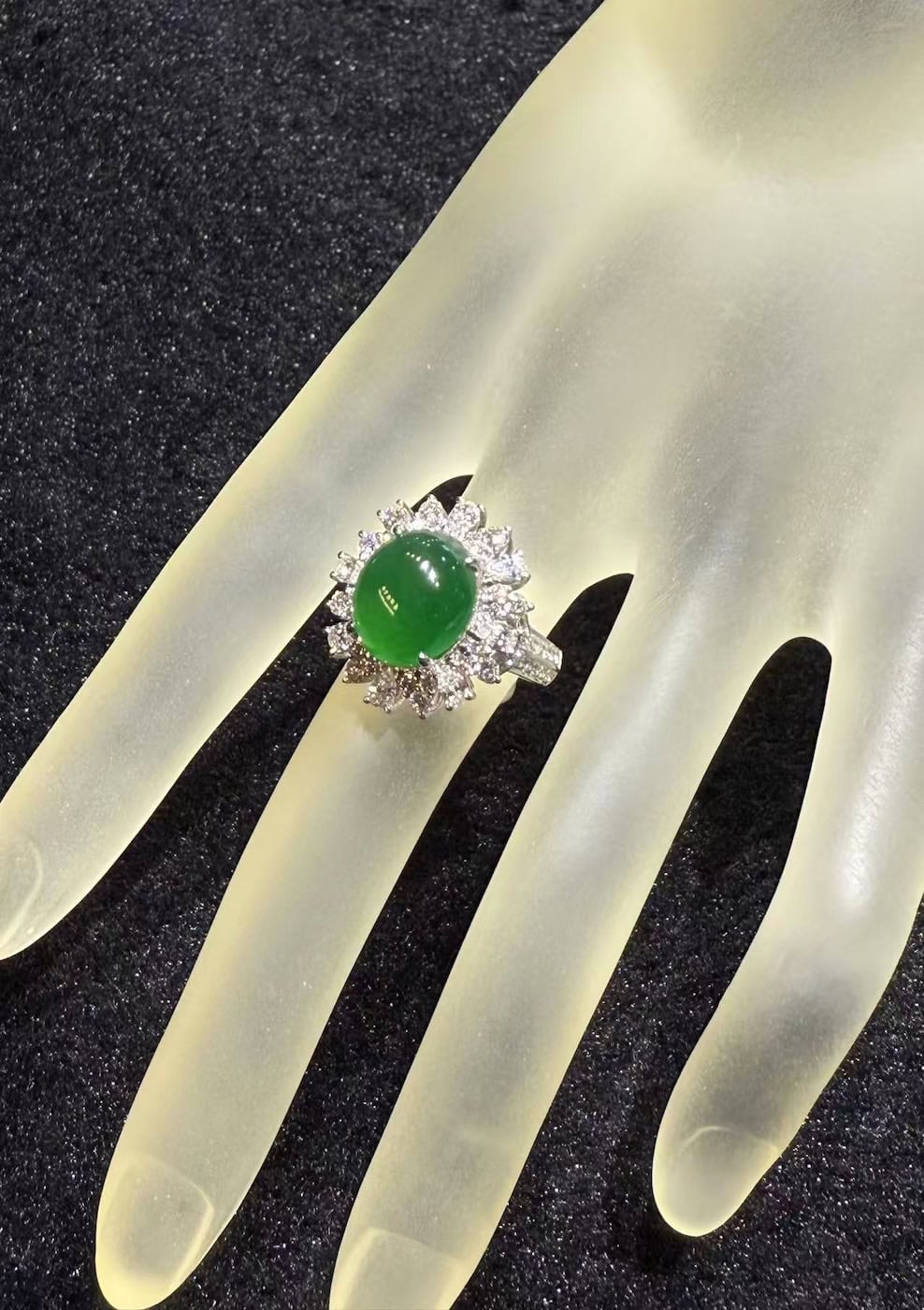 Vivid green jade cabochon ring set in 18k white gold with a brilliant-cut diamond sunburst halo, displayed on a frosted hand stand against black velvet