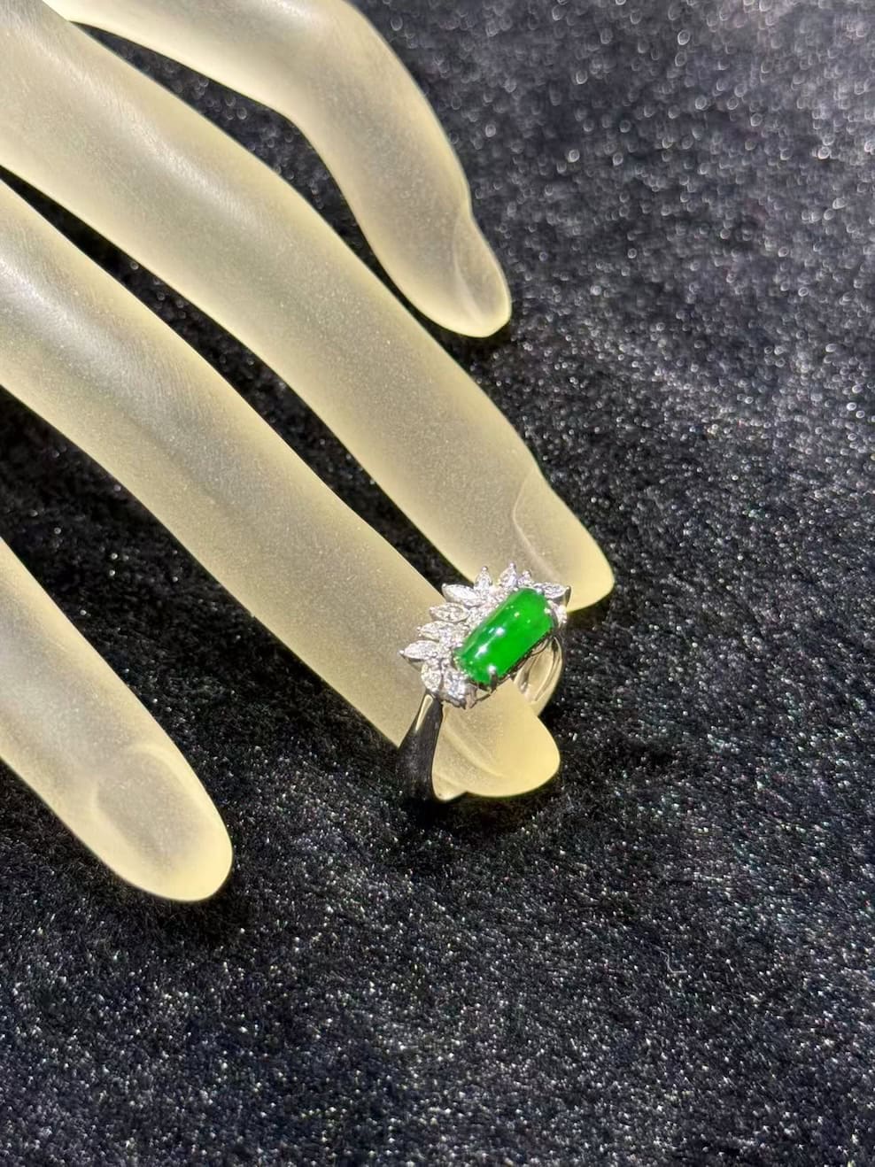 Green jadeite ring with a vivid, almost translucent saddle-shaped cabochon, set in 18k white gold below a fan of marquise-cut diamonds