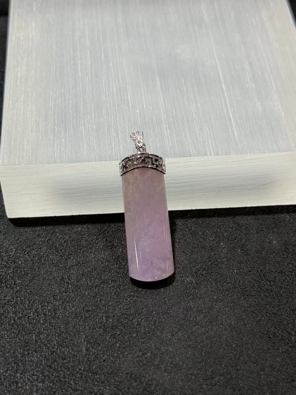 Lavender jade pendant shaped as a smooth uncarved jadeite cylinder, set in 18k white gold with a diamond bail and fretwork cap, displayed on a white stand