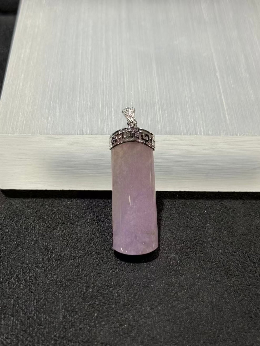 Lavender jade pendant shaped as a smooth uncarved jadeite cylinder, set in 18k white gold with a diamond bail and fretwork cap, displayed on a white stand