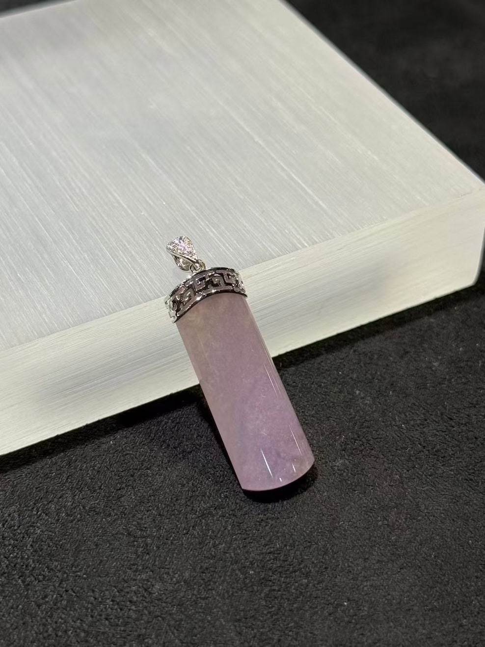 Lavender jade pendant shaped as a smooth uncarved jadeite cylinder, set in 18k white gold with a diamond bail and fretwork cap, displayed on a white stand