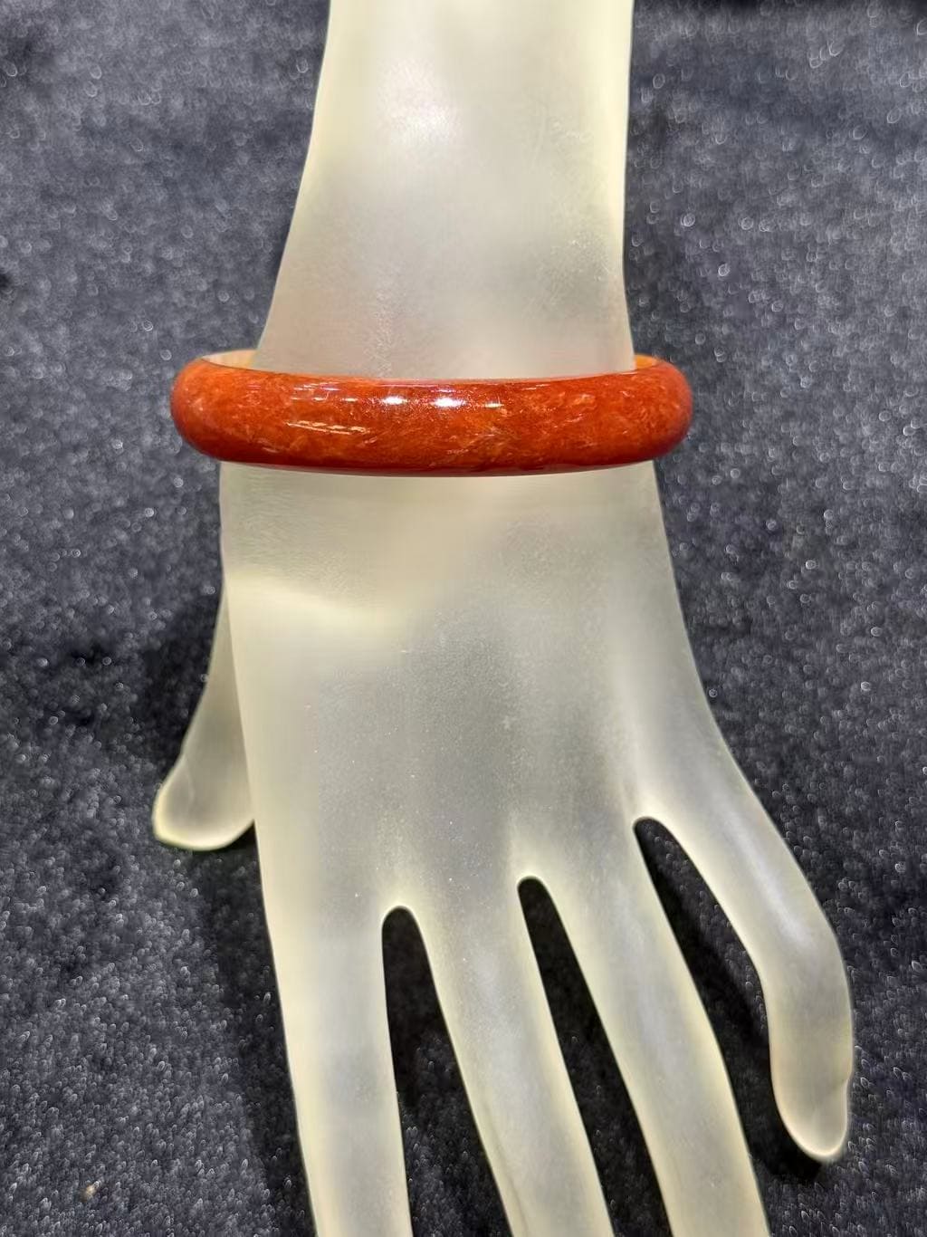Natural red jade bangle in a warm persimmon tone with subtle internal texture, resting on a frosted hand stand against black velvet