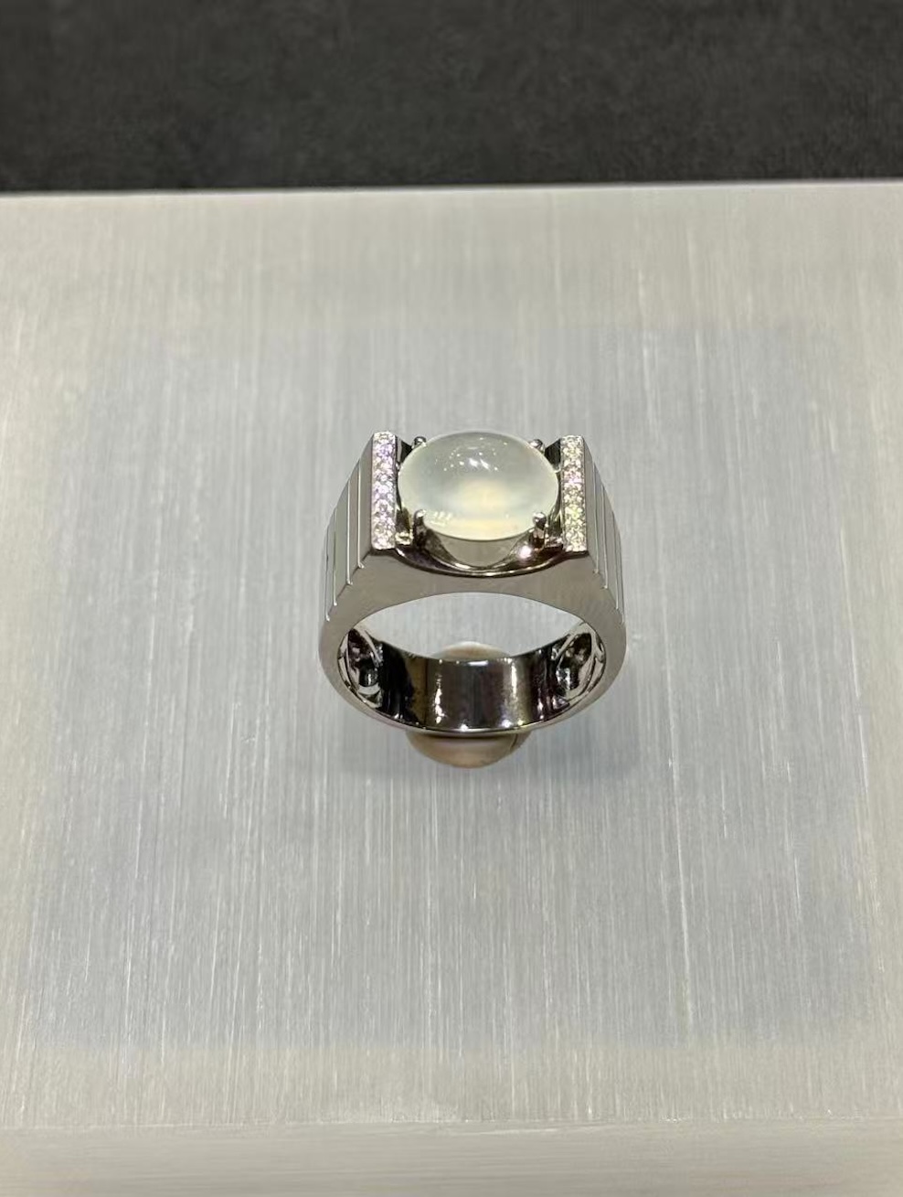 Icy jadeite cabochon ring with a highly translucent, near-colourless oval cabochon set between diamond-lined bars in a wide polished 18k white gold band