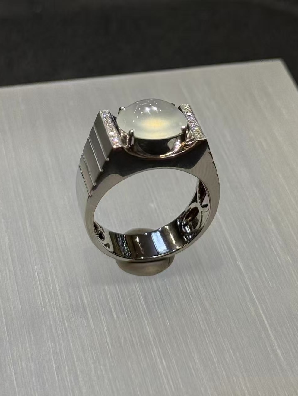 Icy jadeite cabochon ring with a highly translucent, near-colourless oval cabochon set between diamond-lined bars in a wide polished 18k white gold band