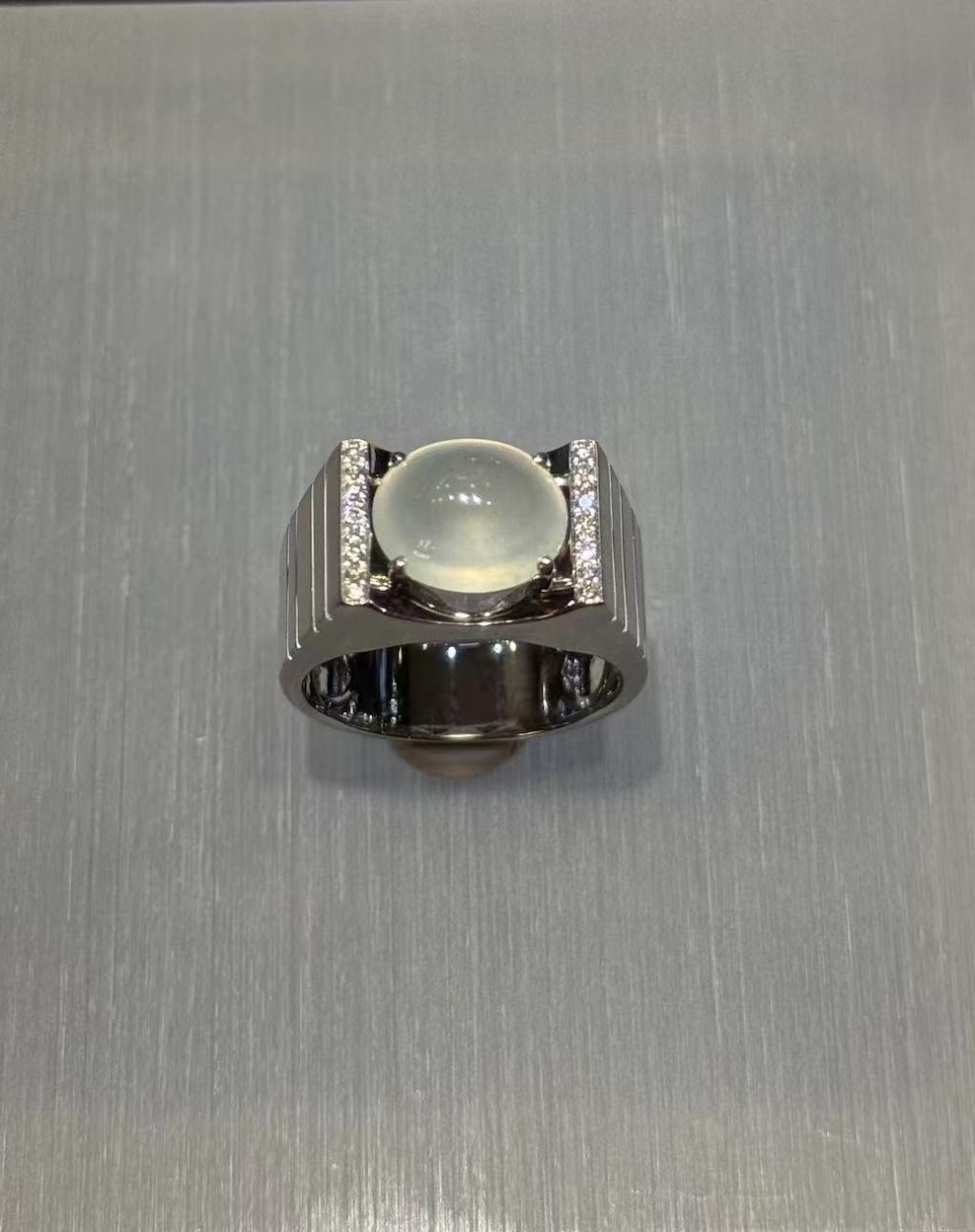 Icy jadeite cabochon ring with a highly translucent, near-colourless oval cabochon set between diamond-lined bars in a wide polished 18k white gold band