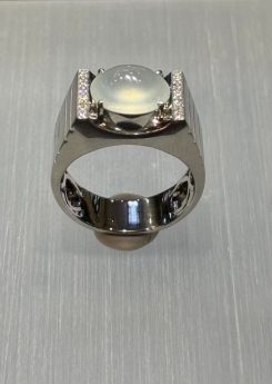 Icy jadeite cabochon ring with a highly translucent, near-colourless oval cabochon set between diamond-lined bars in a wide polished 18k white gold band