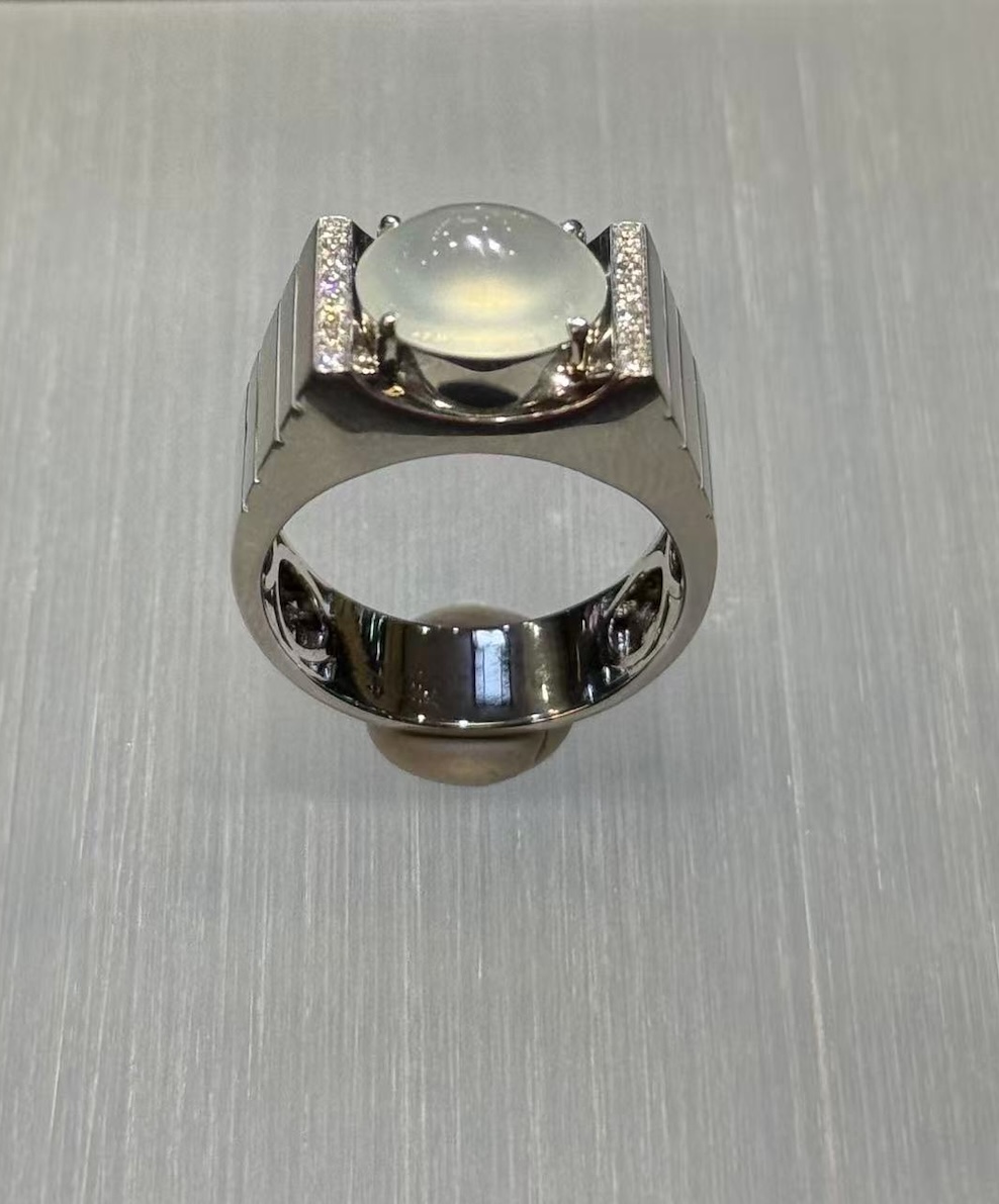 Icy jadeite cabochon ring with a highly translucent, near-colourless oval cabochon set between diamond-lined bars in a wide polished 18k white gold band