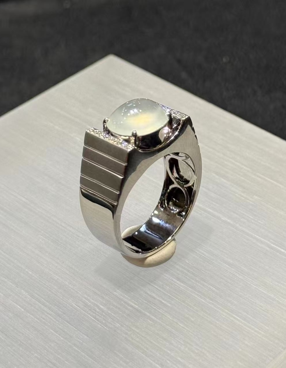 Icy jadeite cabochon ring with a highly translucent, near-colourless oval cabochon set between diamond-lined bars in a wide polished 18k white gold band