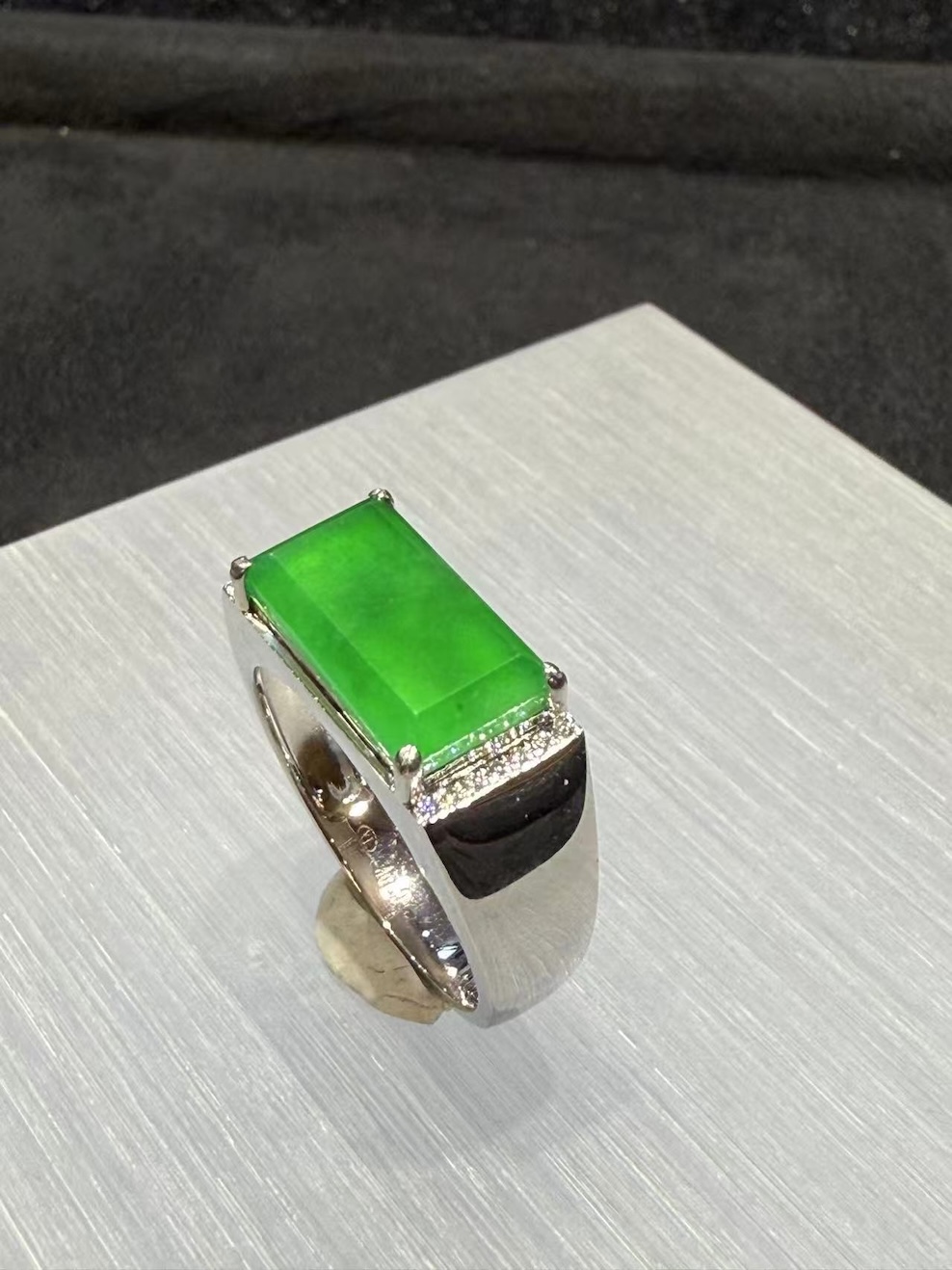 Men's jade ring set with an icy, translucent vibrant green rectangular jadeite cabochon, framed by small diamonds in a wide 18k white gold band