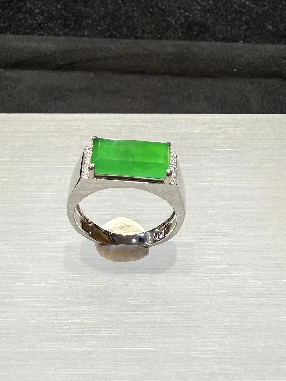 Men's jade ring set with an icy, translucent vibrant green rectangular jadeite cabochon, framed by small diamonds in a wide 18k white gold band