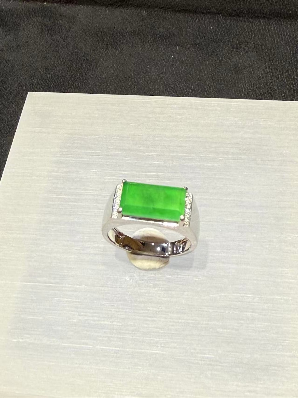 Men's jade ring set with an icy, translucent vibrant green rectangular jadeite cabochon, framed by small diamonds in a wide 18k white gold band