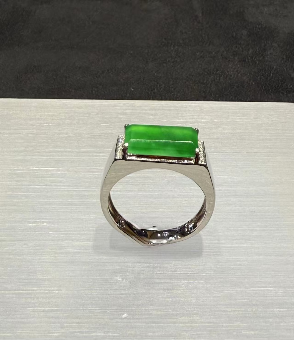 Men's jade ring set with an icy, translucent vibrant green rectangular jadeite cabochon, framed by small diamonds in a wide 18k white gold band