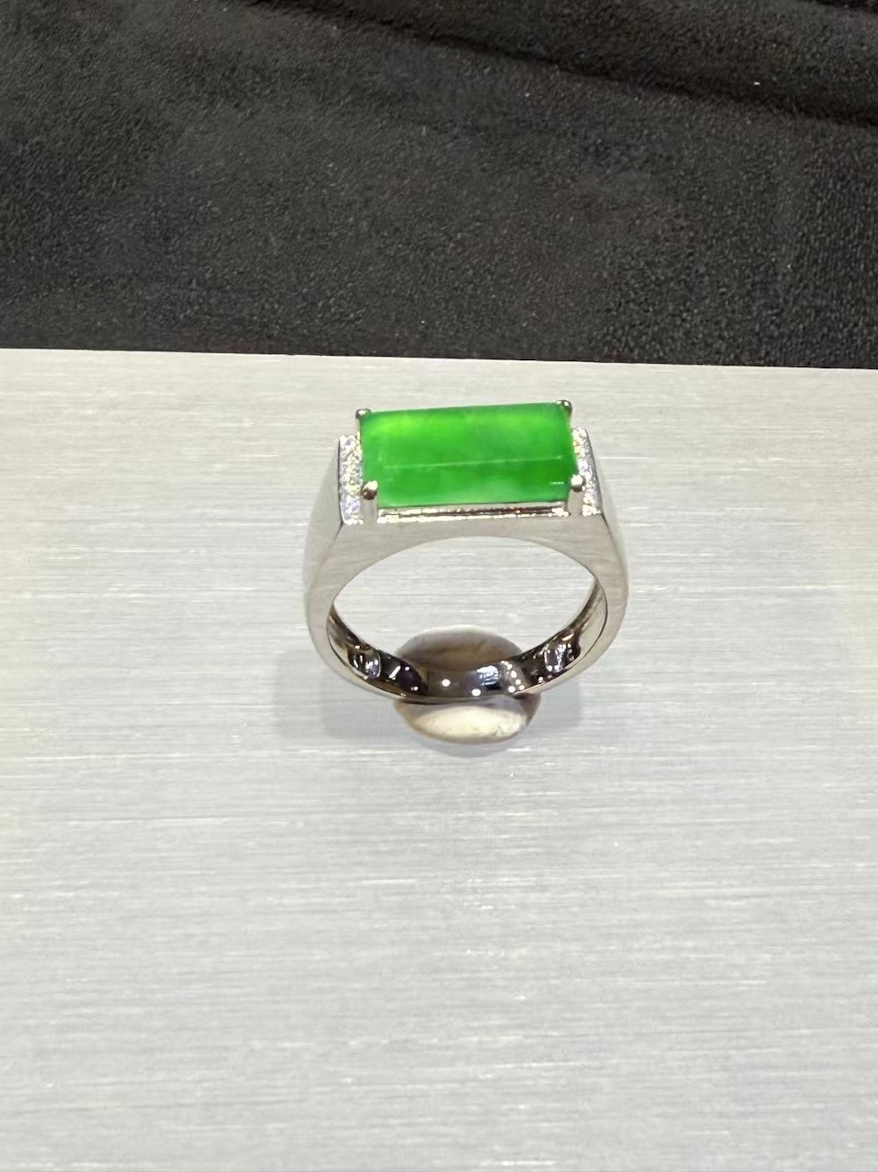 Men's jade ring set with an icy, translucent vibrant green rectangular jadeite cabochon, framed by small diamonds in a wide 18k white gold band