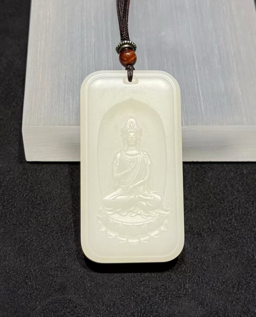 Guanyin nephrite pendant carved from soft white colour, showing the seated Bodhisattva on a lotus within a rectangular pai-zi plaque with a cloud-pattern border, on a black cord