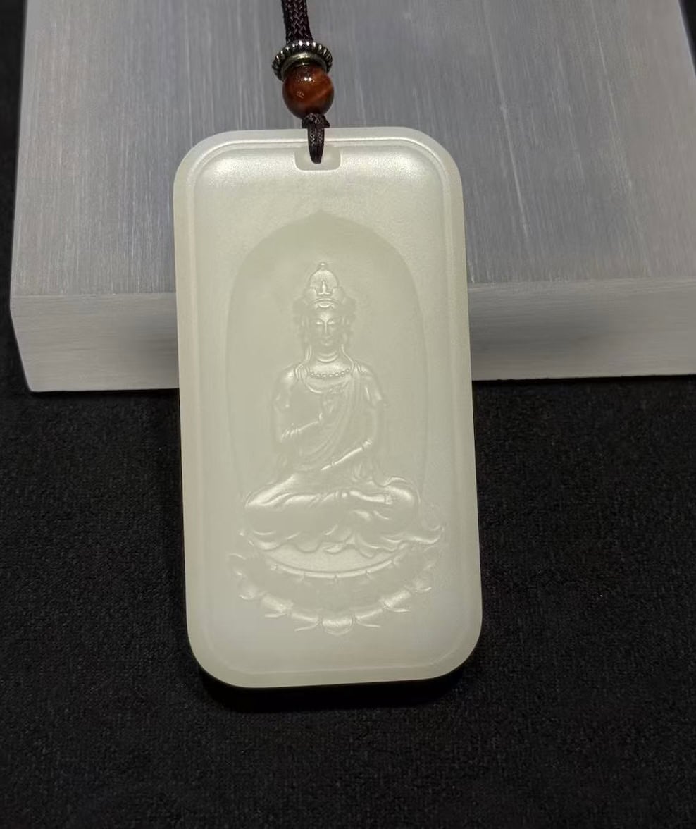 Guanyin nephrite pendant carved from soft white colour, showing the seated Bodhisattva on a lotus within a rectangular pai-zi plaque with a cloud-pattern border, on a black cord