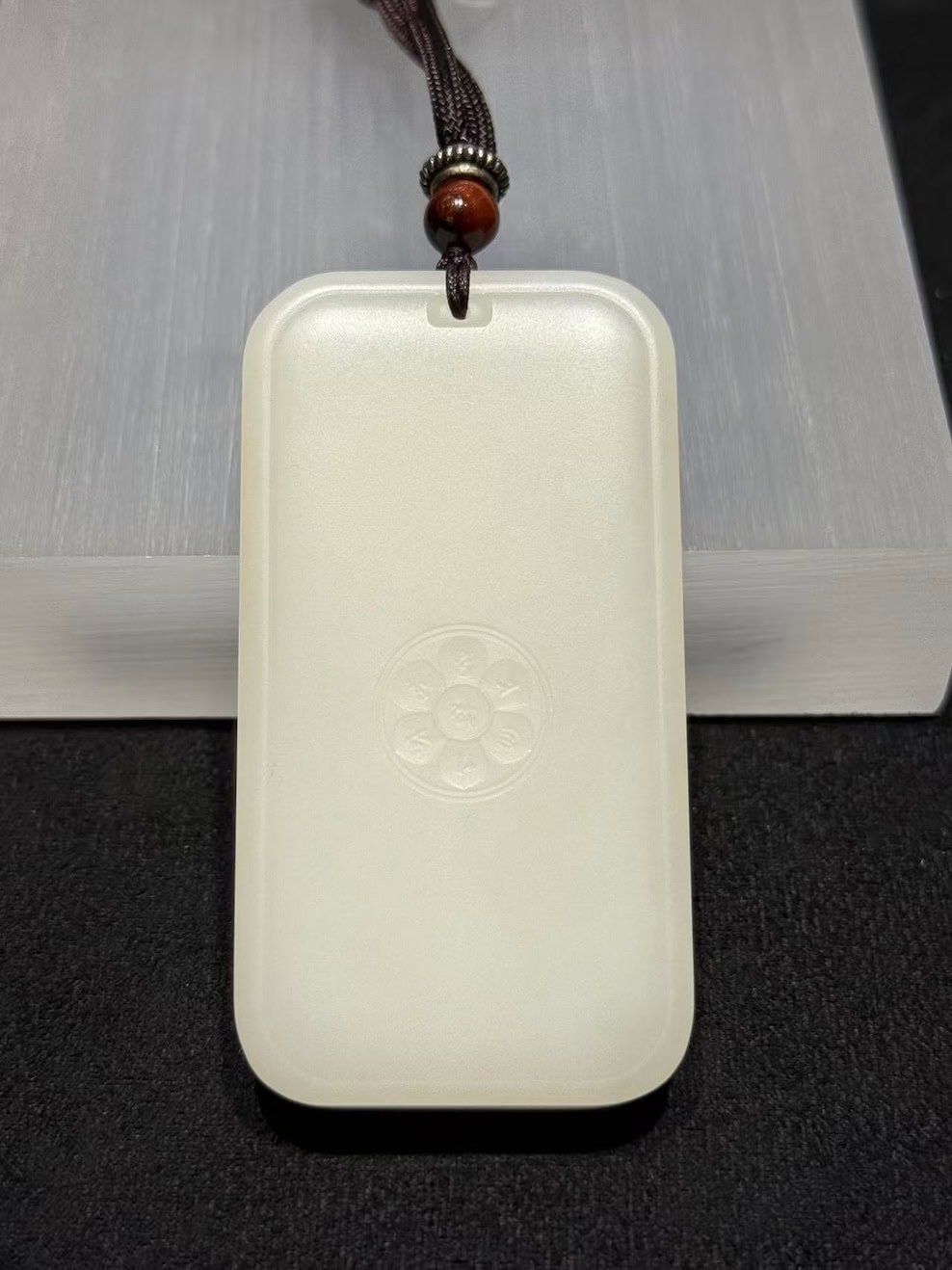 Guanyin nephrite pendant carved from soft white colour, showing the seated Bodhisattva on a lotus within a rectangular pai-zi plaque with a cloud-pattern border, on a black cord