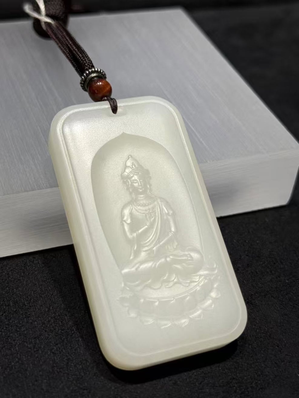 Guanyin nephrite pendant carved from soft white colour, showing the seated Bodhisattva on a lotus within a rectangular pai-zi plaque with a cloud-pattern border, on a black cord