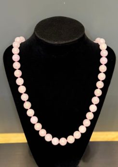 Lavender jade necklace strung with round translucent faint pink-lavender jadeite beads, shown on a black necklace display bust