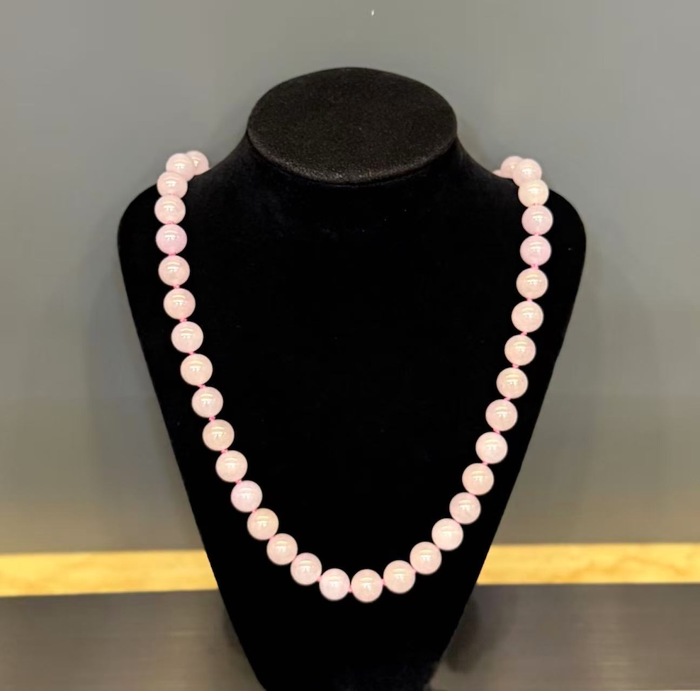 Lavender jade necklace strung with round translucent faint pink-lavender jadeite beads, shown on a black necklace display bust
