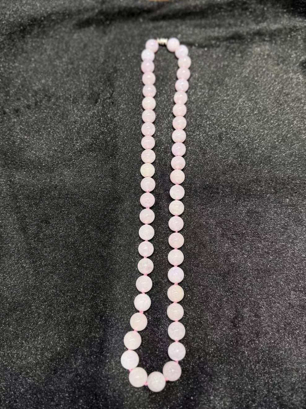 Lavender jade necklace strung with round translucent faint pink-lavender jadeite beads, shown on a black necklace display bust
