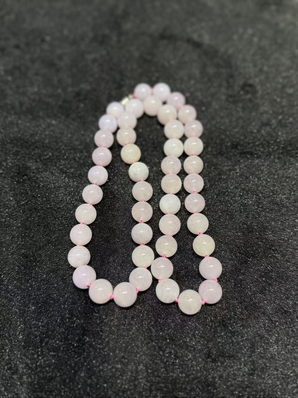 Lavender jade necklace strung with round translucent faint pink-lavender jadeite beads, shown on a black necklace display bust