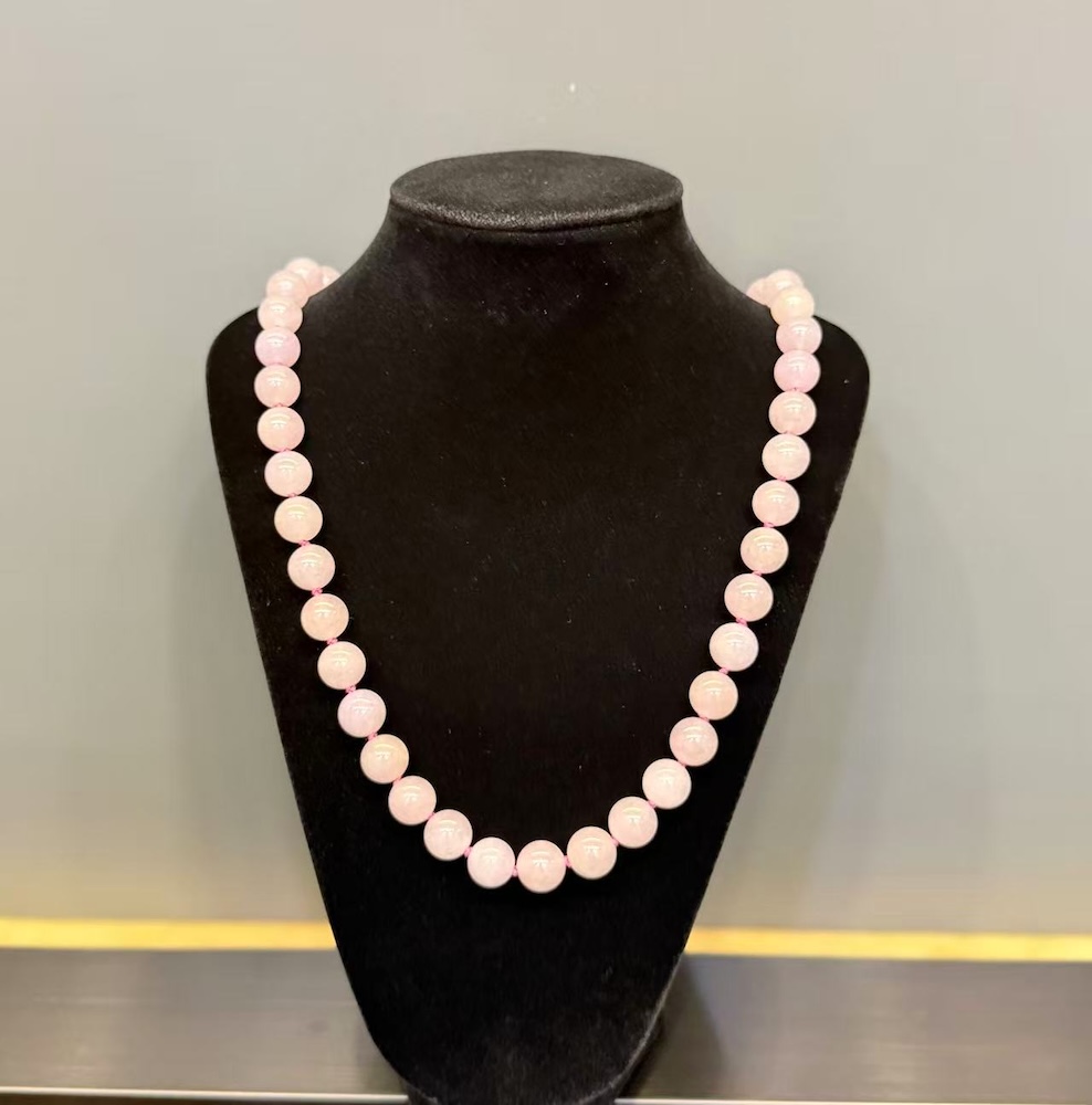 Lavender jade necklace strung with round translucent faint pink-lavender jadeite beads, shown on a black necklace display bust