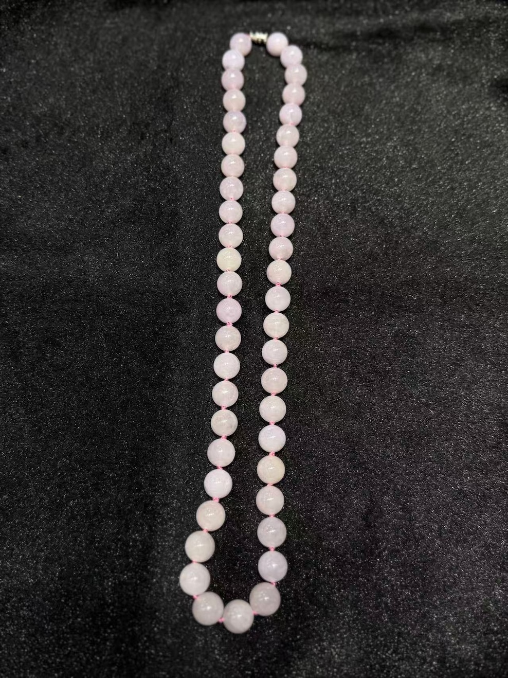 Lavender jade necklace strung with round translucent faint pink-lavender jadeite beads, shown on a black necklace display bust