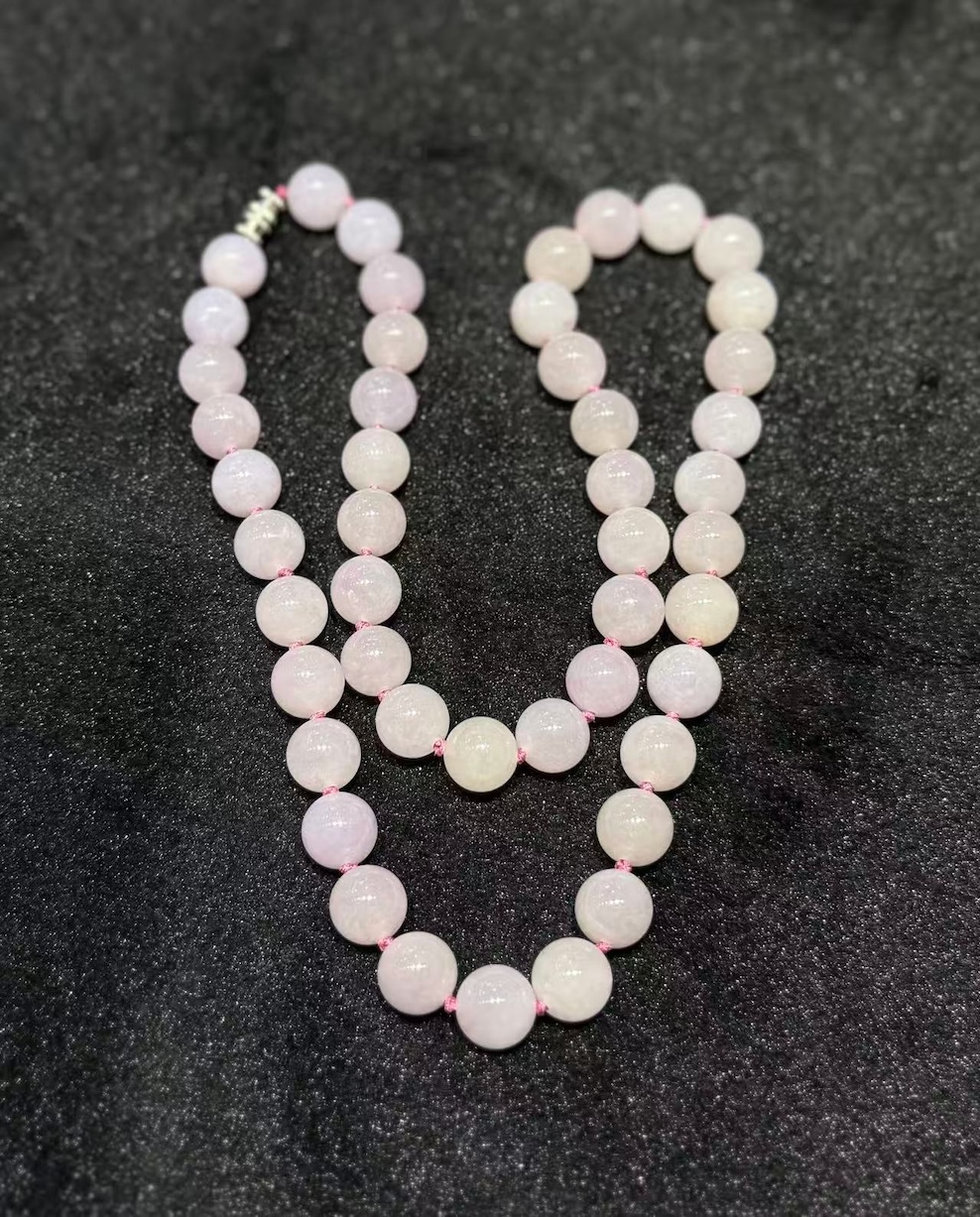 Lavender jade necklace strung with round translucent faint pink-lavender jadeite beads, shown on a black necklace display bust