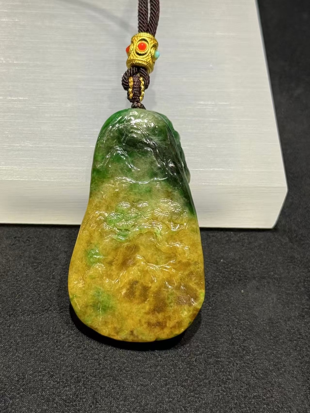 Tiger jade pendant carved from translucent yellow and green jadeite, with a detailed tiger head at the centre, a lotus blossom at the base, and openwork scrollwork above, hung on a brown rope with a small brass bead