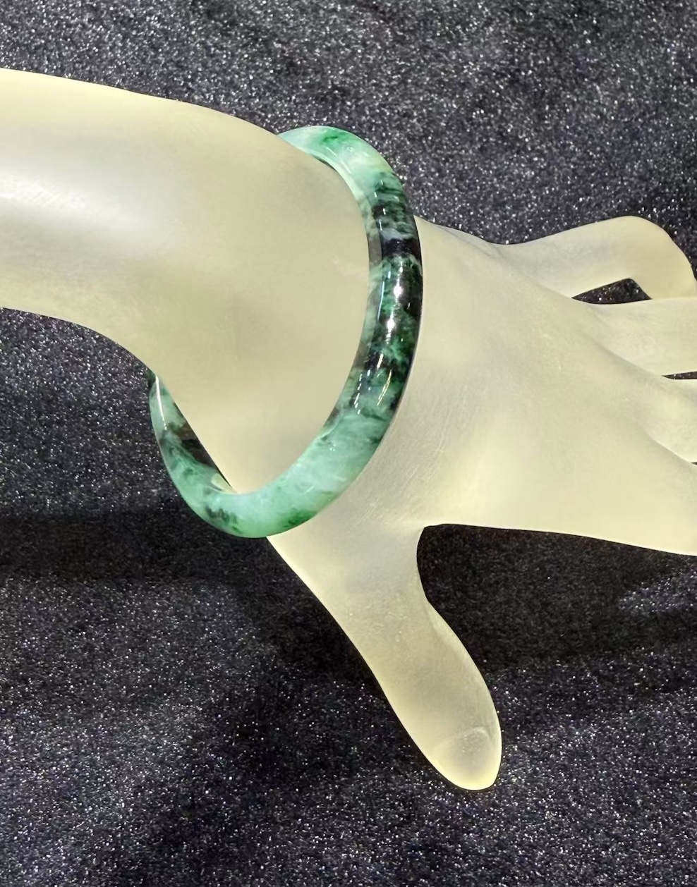 Old pit jadeite bangle in an oval shape, with translucent green jadeite carrying deeper green patches and natural dark inclusions