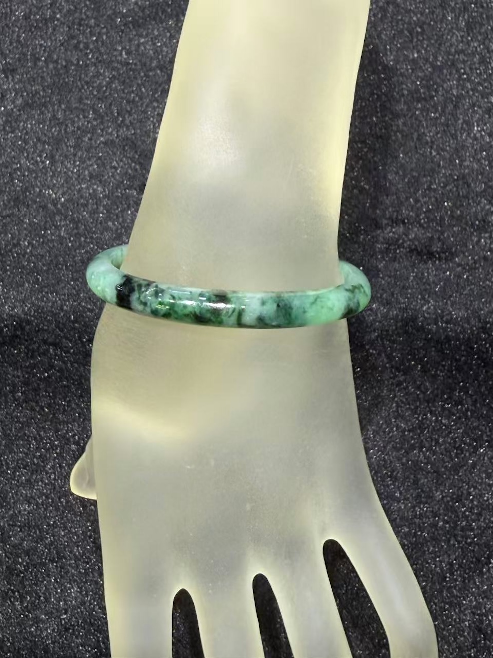Old pit jadeite bangle in an oval shape, with translucent green jadeite carrying deeper green patches and natural dark inclusions