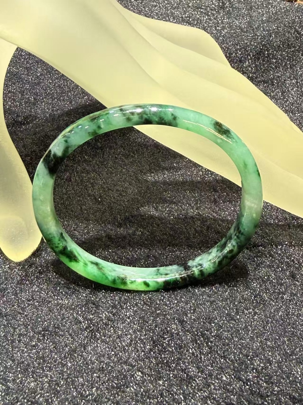 Old pit jadeite bangle in an oval shape, with translucent green jadeite carrying deeper green patches and natural dark inclusions